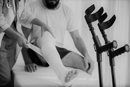 man with crutches having his injured leg bandaged by doctor