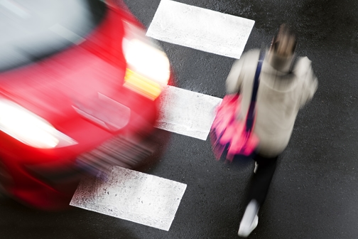 blurred image of red vehicle approaching pedestrian in crosswalk